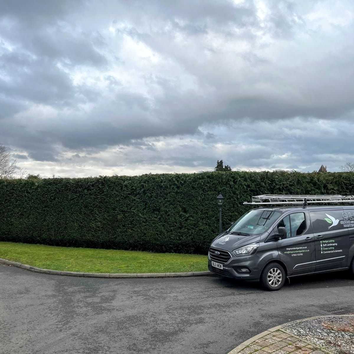 A BLS Ground & Garden van parked beside a long, neatly trimmed hedge.