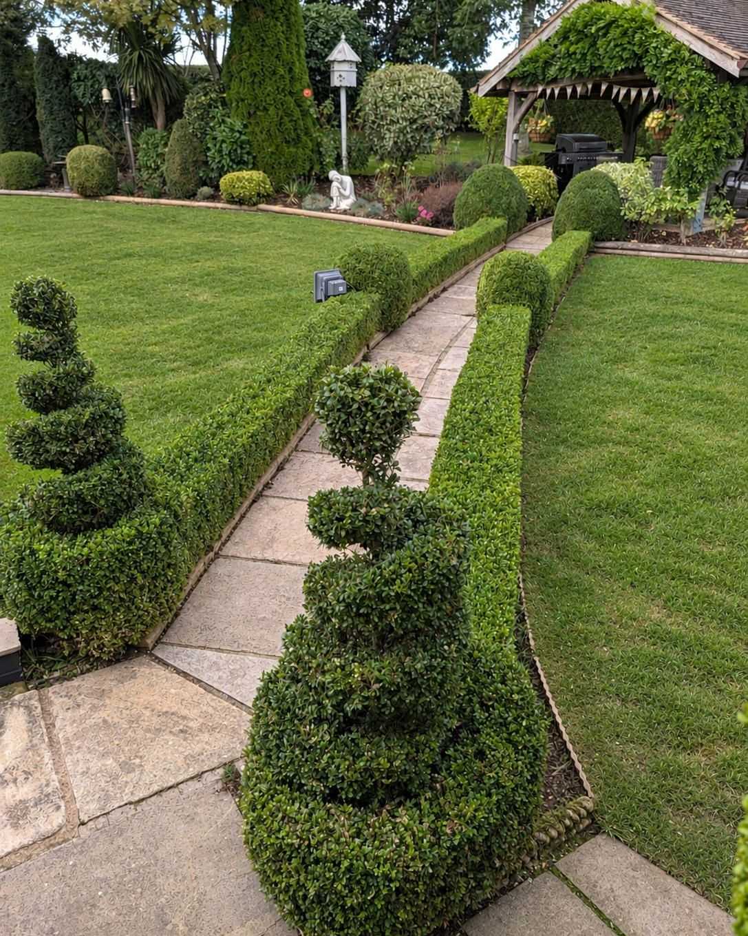 A paved garden path between neat lawns and spiral-clipped topiary.