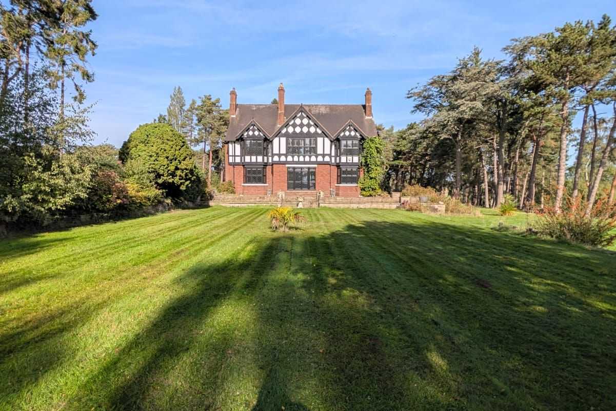 A large striped lawn leading up to a Tudor-style house.
