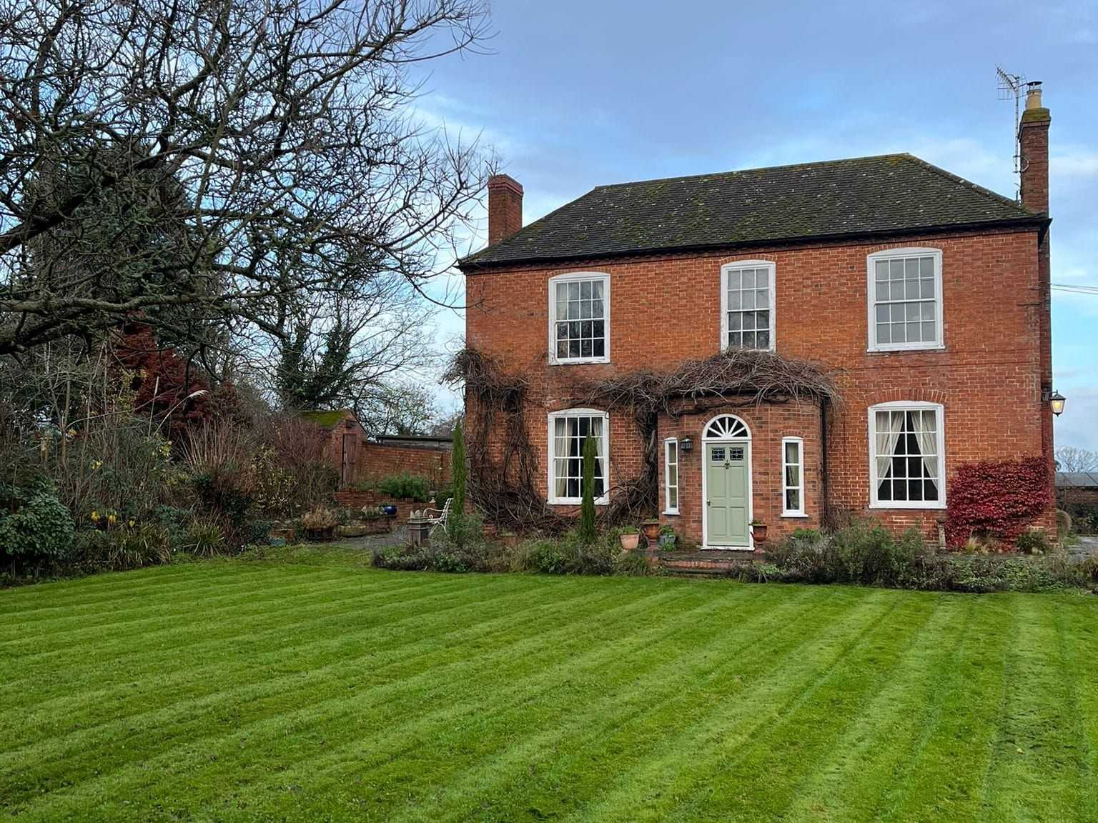 A striped lawn in front of a red-brick house on a sunny day.