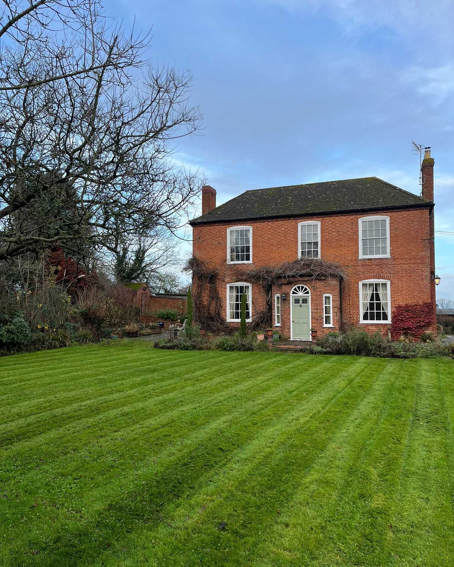 A striped lawn in front of a red-brick house on a sunny day.