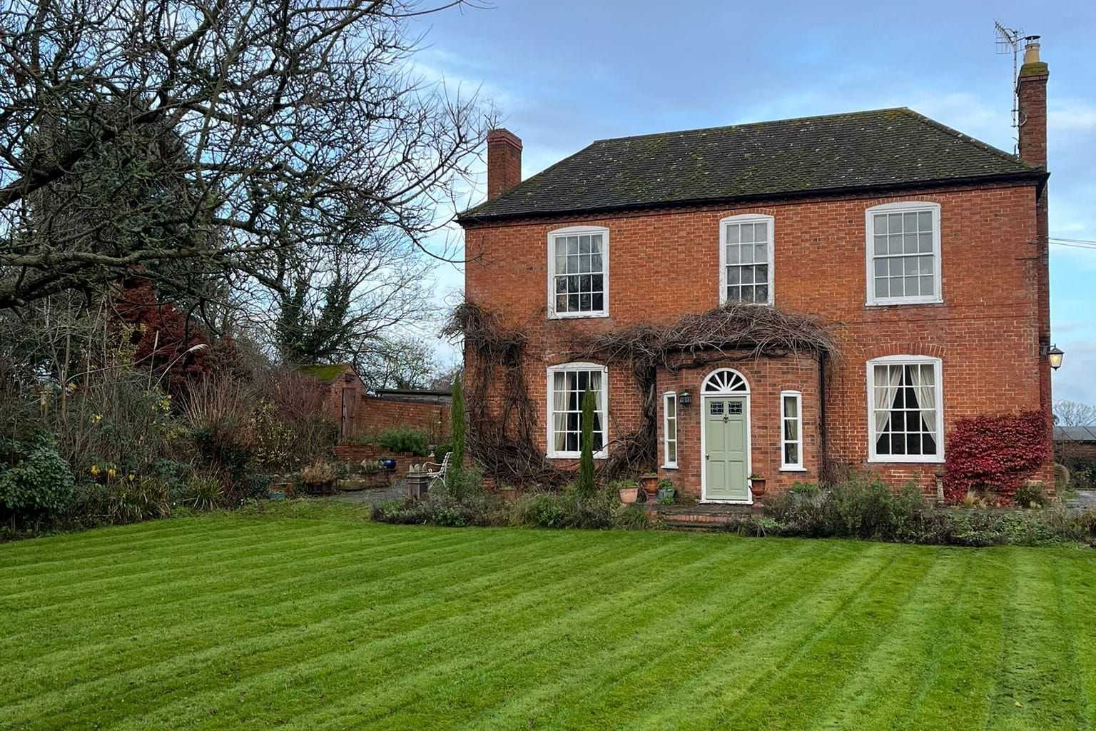 A striped lawn in front of a red-brick house on a sunny day.